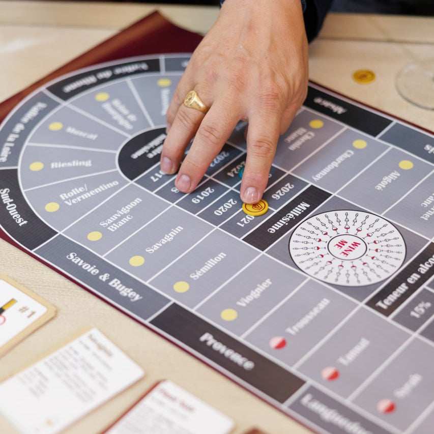 Gros plan sur le plateau du jeu Wine Me avec un joueur déplaçant un pion, entouré de cartes et de jetons de jeu.
